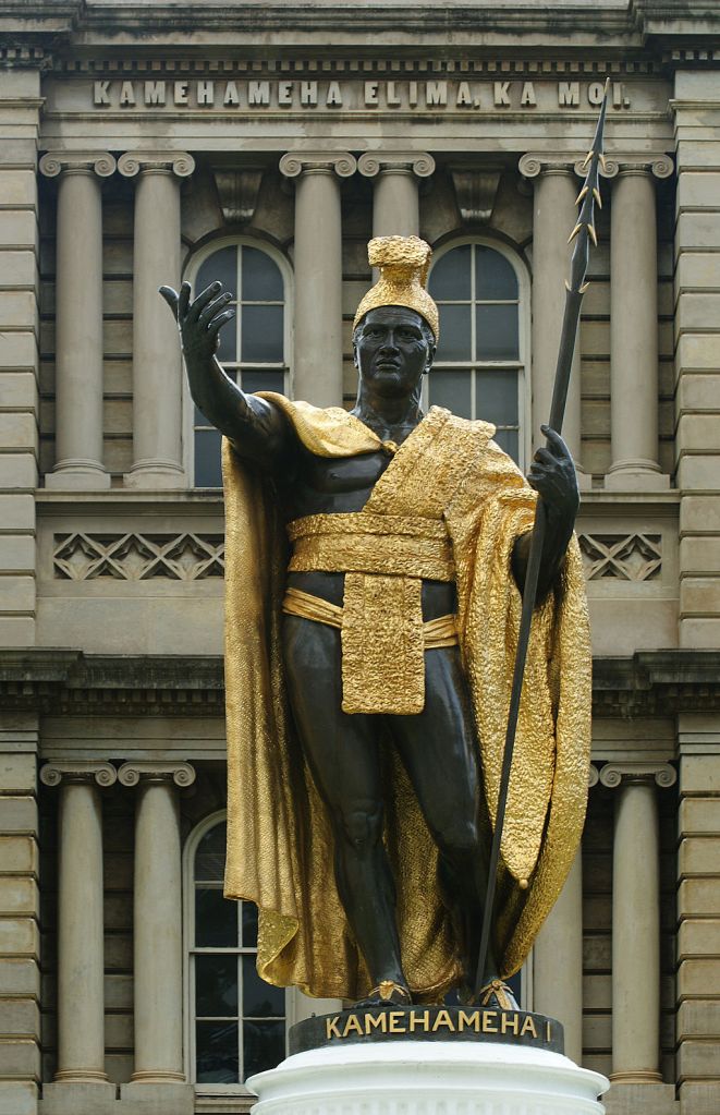 Statue of King Kamehameha I, standing in front of Ali'iolani Hale in Honolulu. Cast: 1881, bronze with gold leaf. This was the second casting due to the first going down in a shipwreck (later recovered and on display in Kapaʻua. Approx 8½ feet tall on a 10 foot concrete base. The pedestal has four bronze and gold leaf plaques with scenes from Kamehameha's life. Sculptor: Thomas Ridgeway Gould (1818–1881).